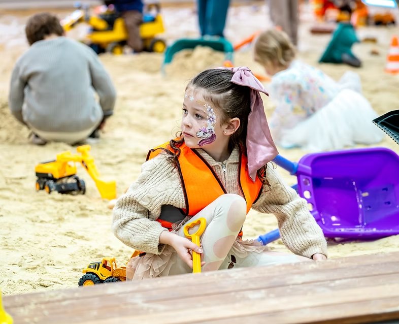 Girl with face paint playing with a toy digger in the sand