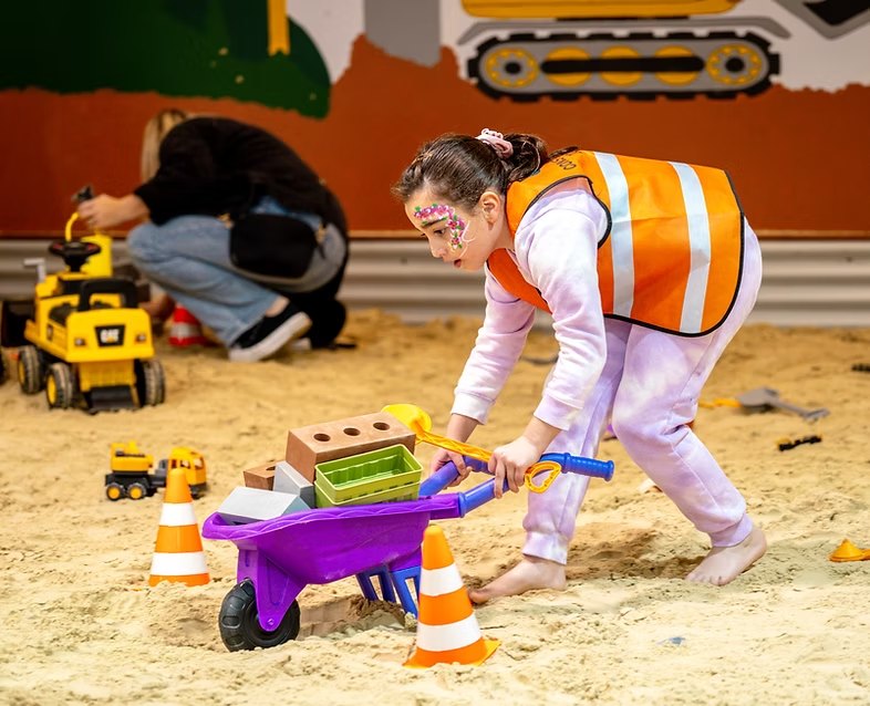 Child in a hi-vis vest pushing a wheelbarrow of bricks